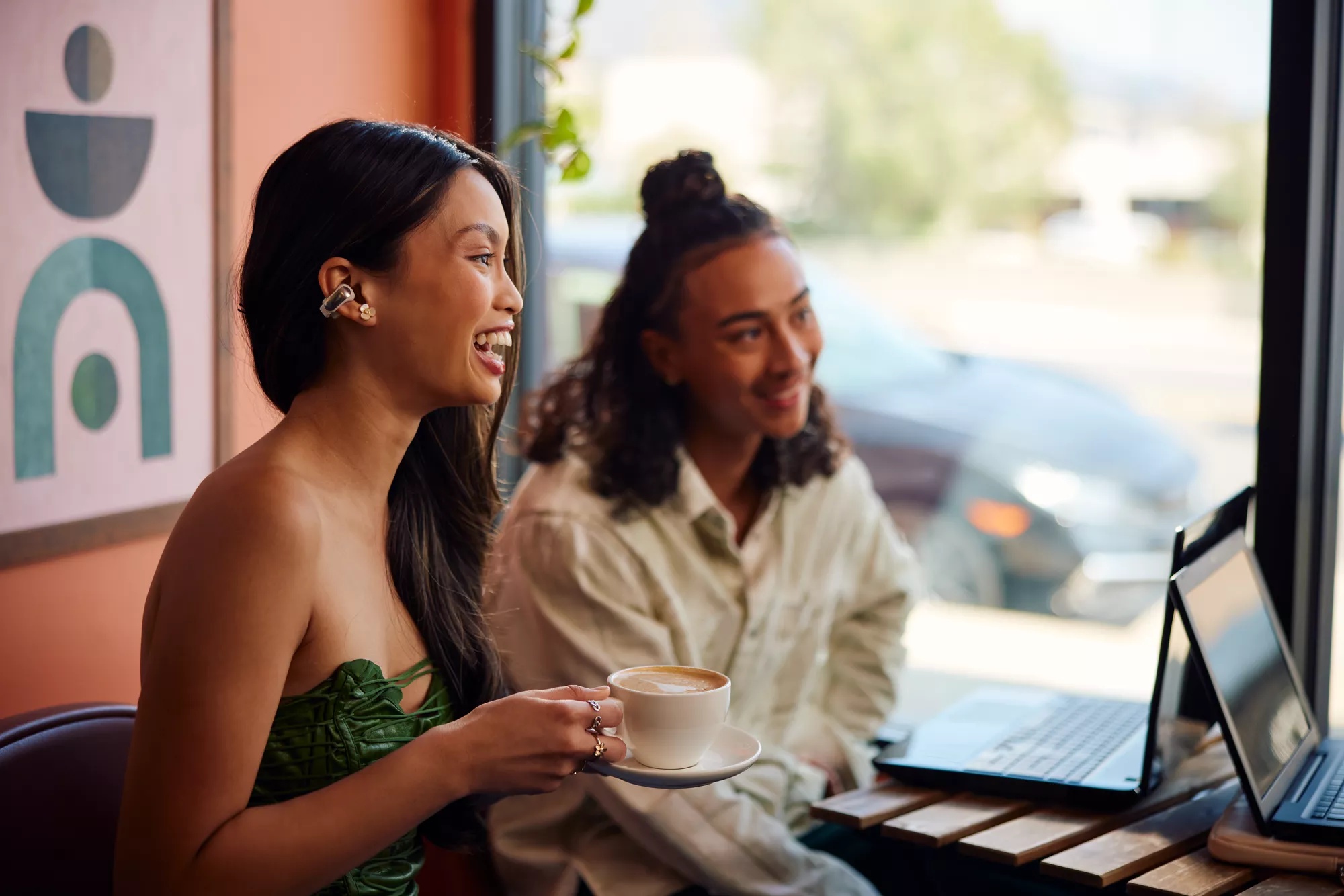 Woman wearing Bose Ultra Open Earbuds in a cafe with friends having coffee.