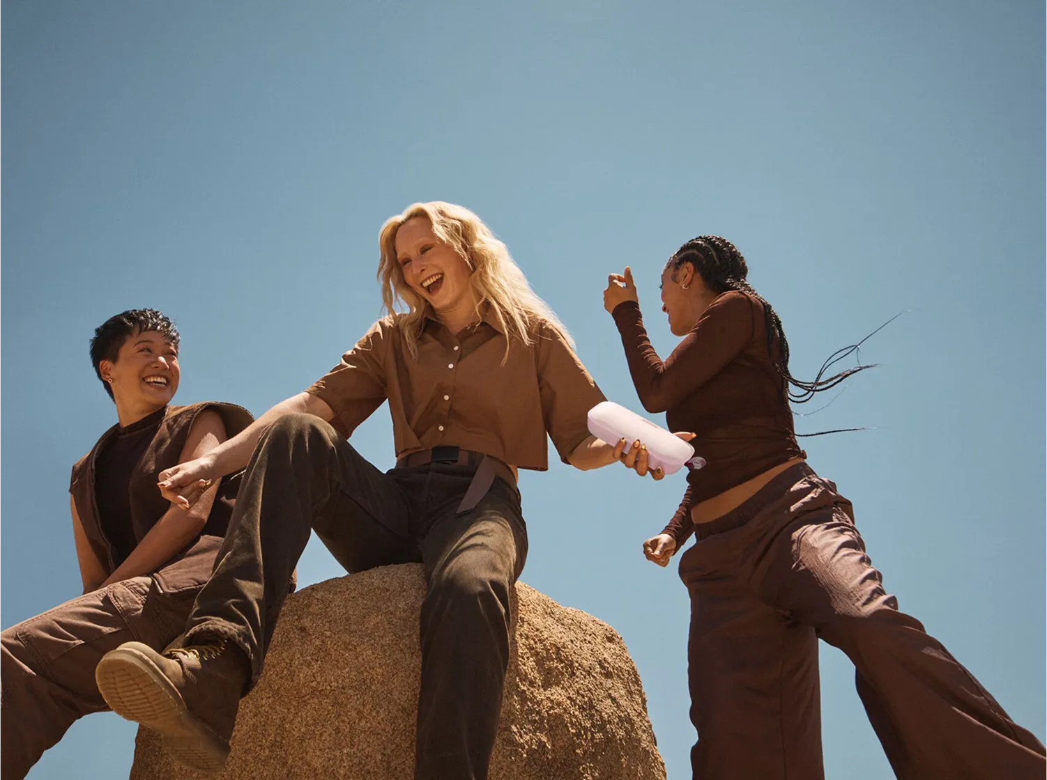 Three friends sitting on a rock listening to a Bose SoundLink Flex Portable Speaker (2nd Gen) in Petal Pink.